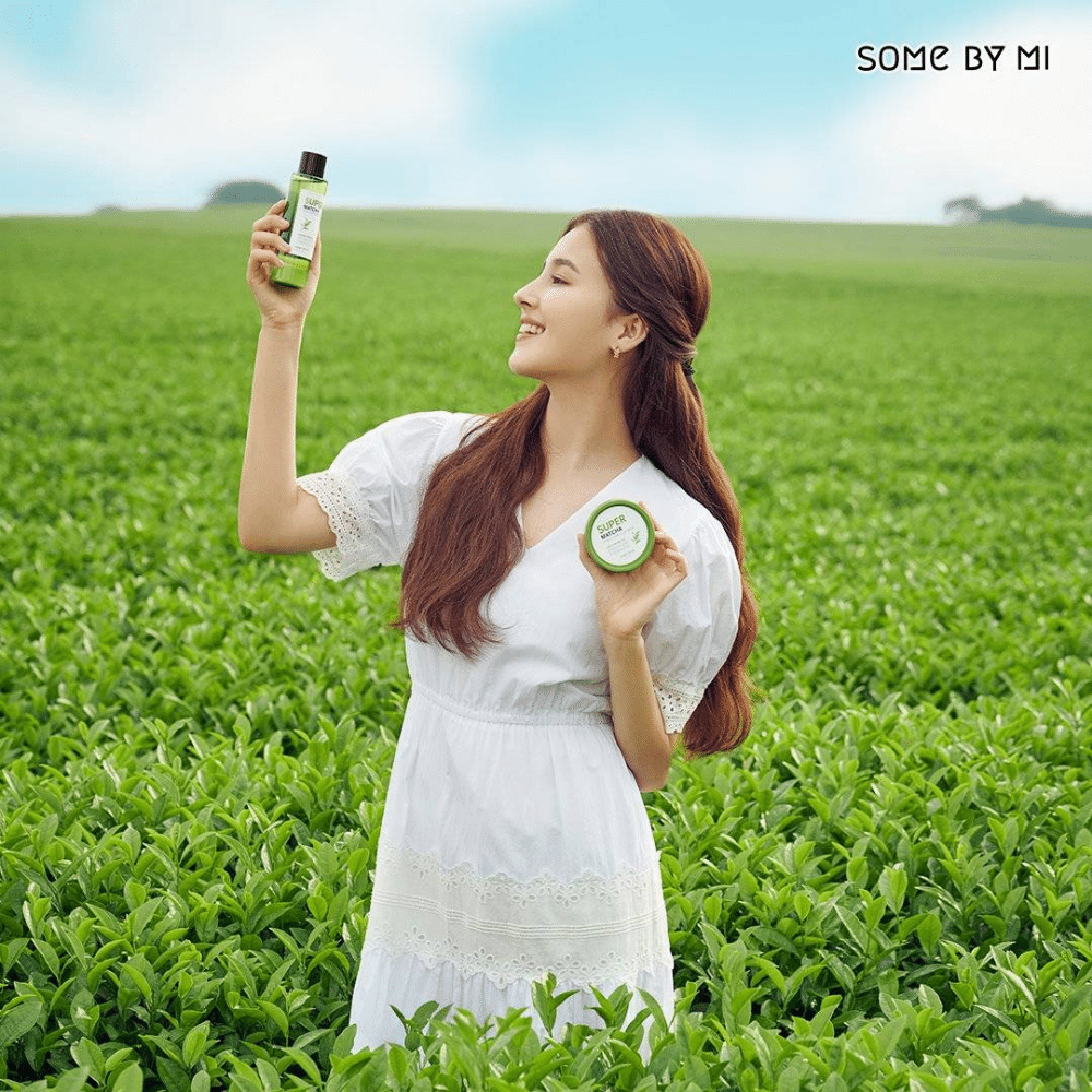En kvinna som håller i en flaska SOME BY MI Super Matcha Pore Tightening Toner 150ml på ett fält.